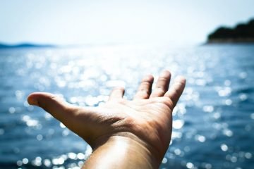 person hand reaching body of water